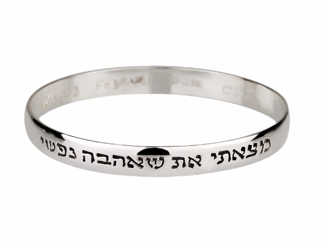 A silver bangle with hebrew writing on it.