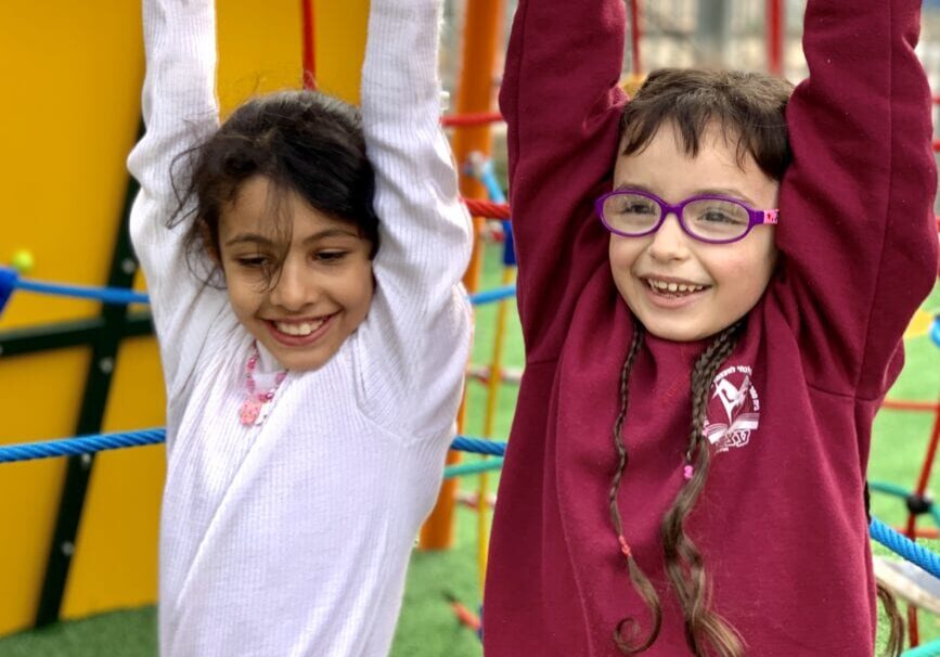 Two children hanging from a metal bar in the park.